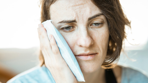 Woman holding an ice pack to her jaw in pain, needing an emergency dentist in Sydney